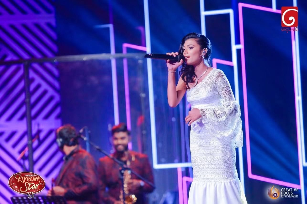 Kawya Erandi performing on the Derana Dream Star stage in a white lace gown