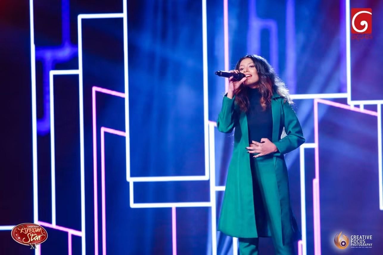 Kawya Erandi performing live on stage in green coat